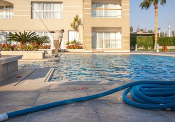 Backyard swimming pool with pool vacuum and maintenance supplies on the pool deck